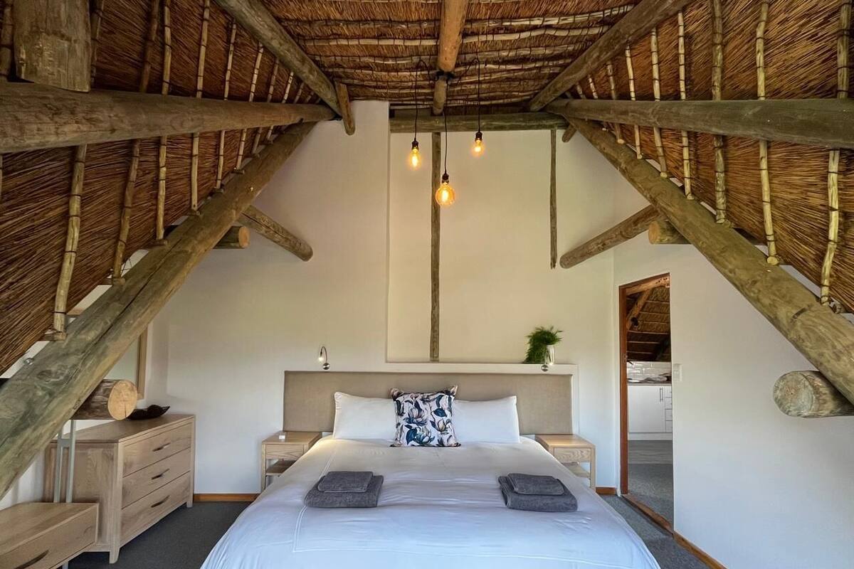 A bedroom with a bed, bedside tables, a nightstand, a wooden dresser, a headboard, and a ceiling with exposed beams.