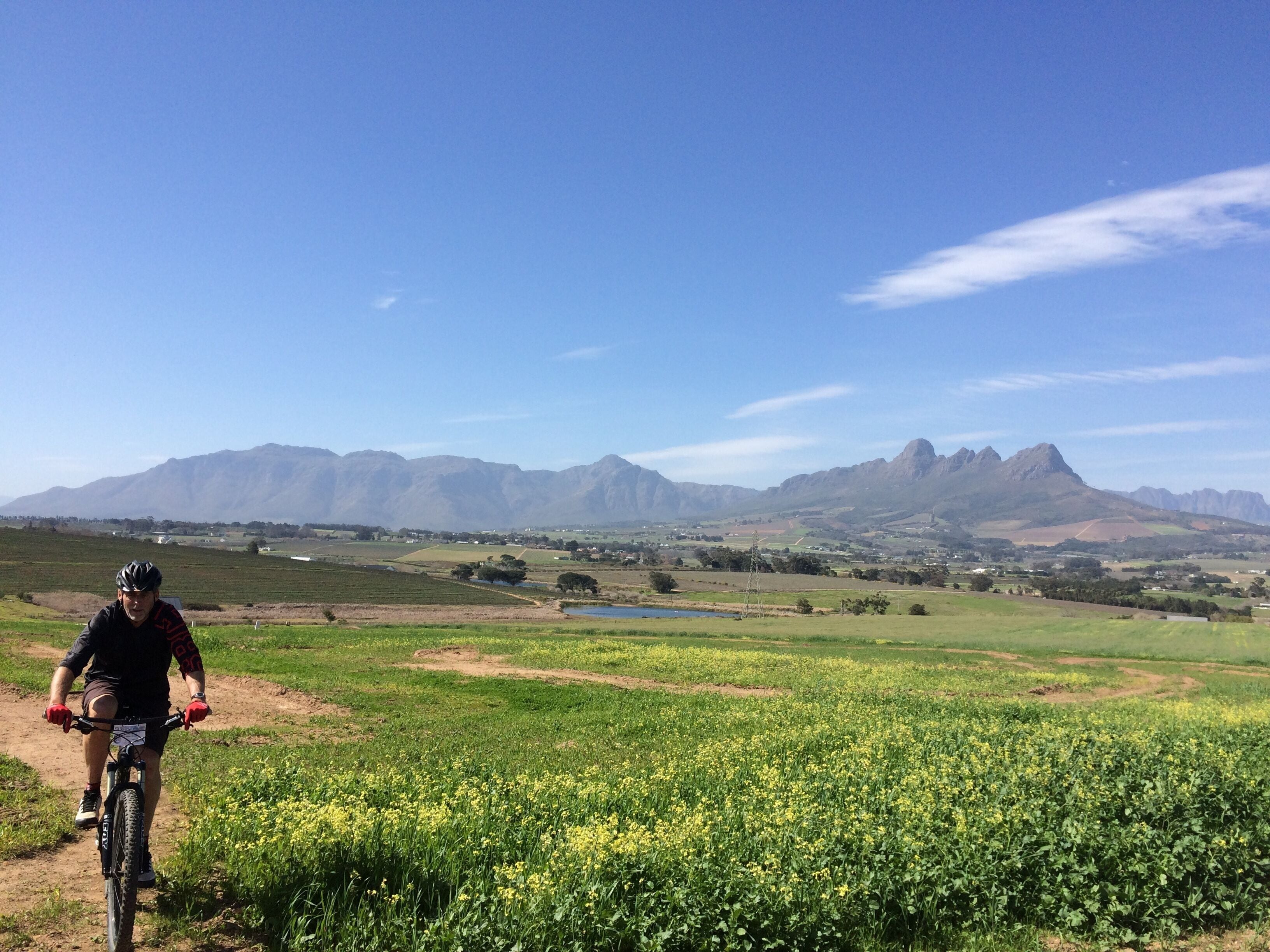 A cyclist on a dirt path with fields and mountains in the background.