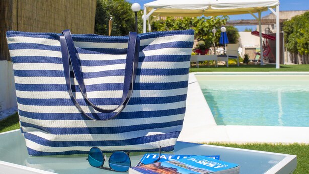 A striped bag on a table with a book and sunglasses. - Migair (Misiliscemi)
