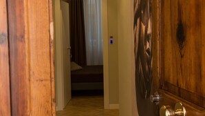 A wooden door with a brass handle, a wooden floor, and a hallway leading to a room with a bed and curtains. - Le Affacciate Bruzie Home (Cosenza)