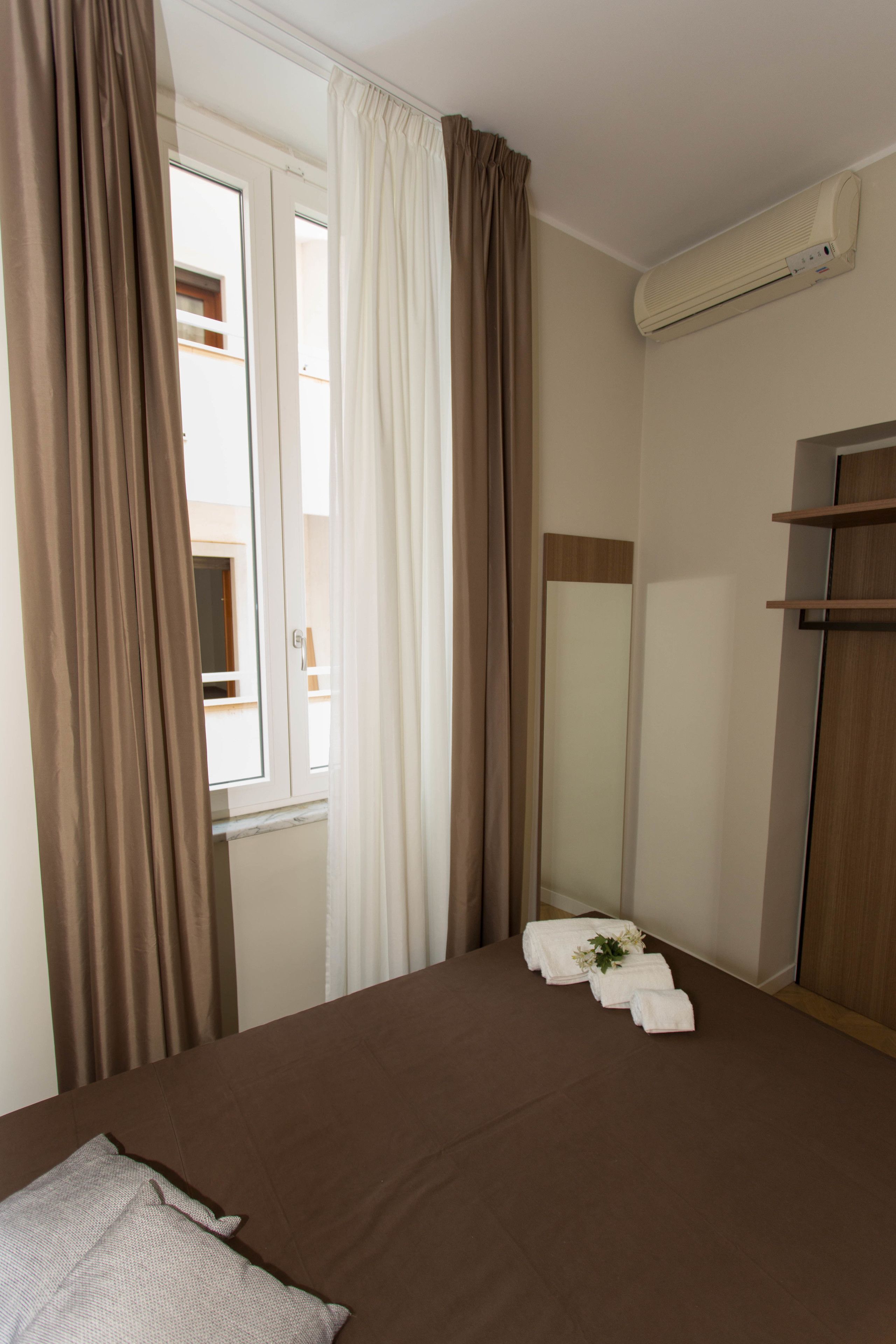 Een hotelkamer met een bed, een spiegel, een raam met gordijnen en een airconditioning.
