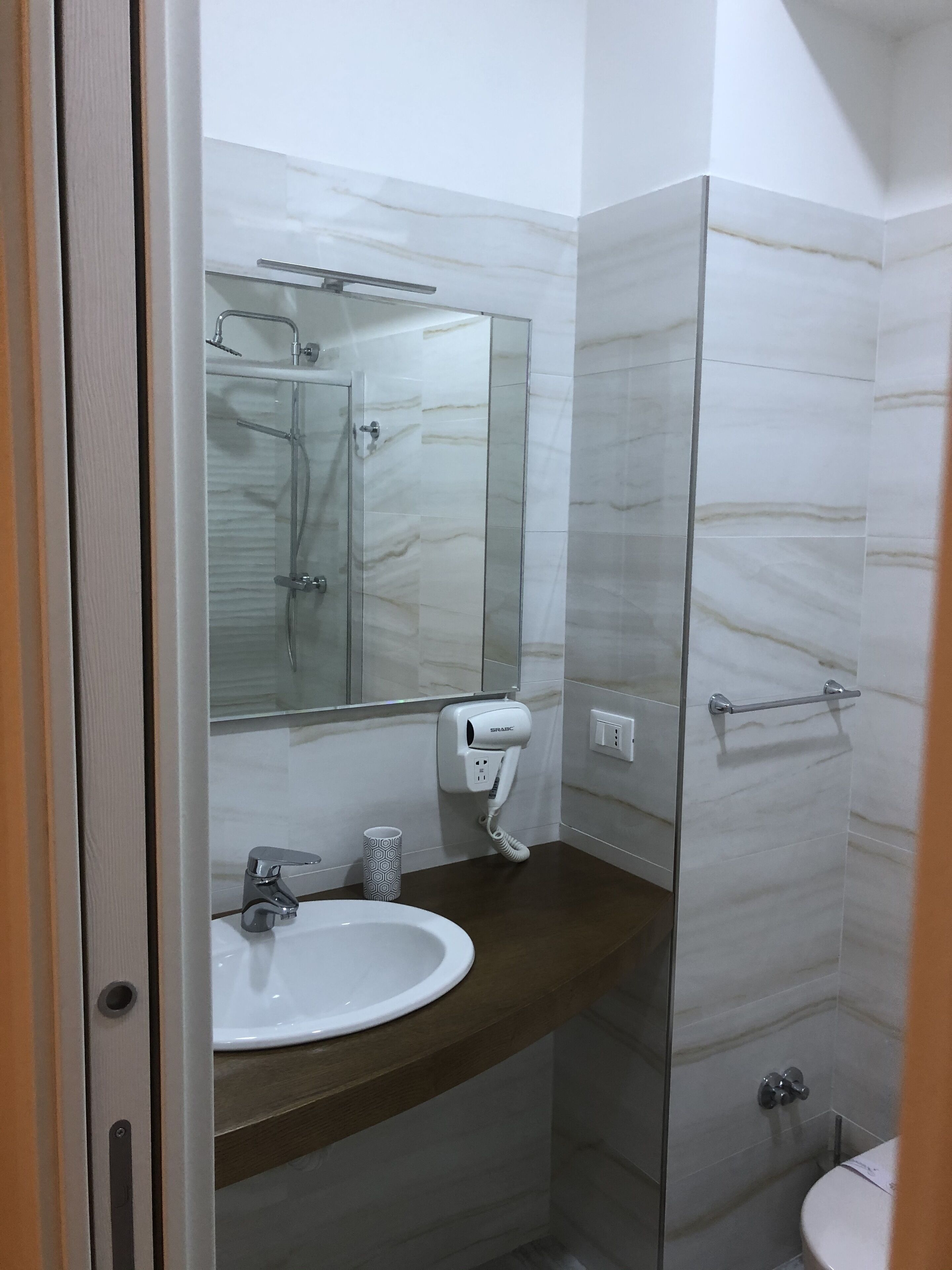 Ein Badezimmer mit Marmorwand, einer Duschkabine aus Glas, einem weißen Waschbecken und einer Toilette.