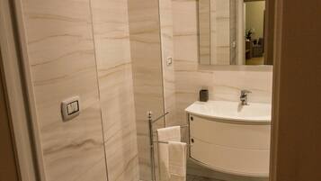 Une salle de bain moderne avec un sol en marbre, un lavabo rond et une cabine de douche en verre.