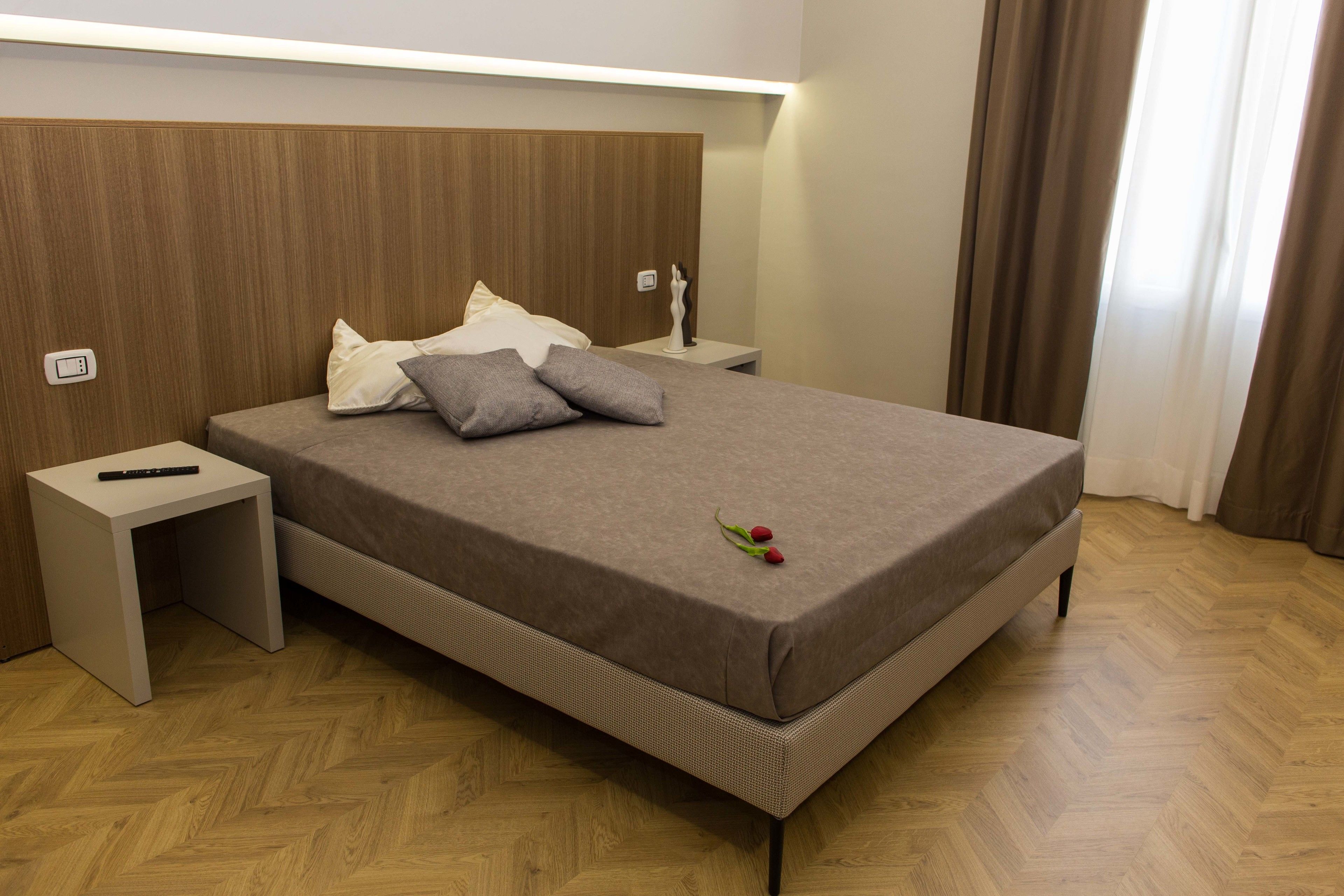 A neatly made bed with a brown headboard, a bedside table with a remote control, and a small decorative item on the bed.