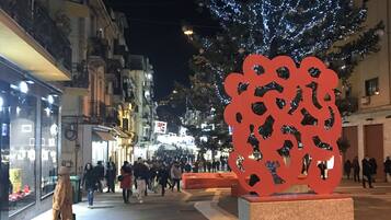 A public square with a decorative metal sculpture, a tree adorned with lights, and a crowd of people.