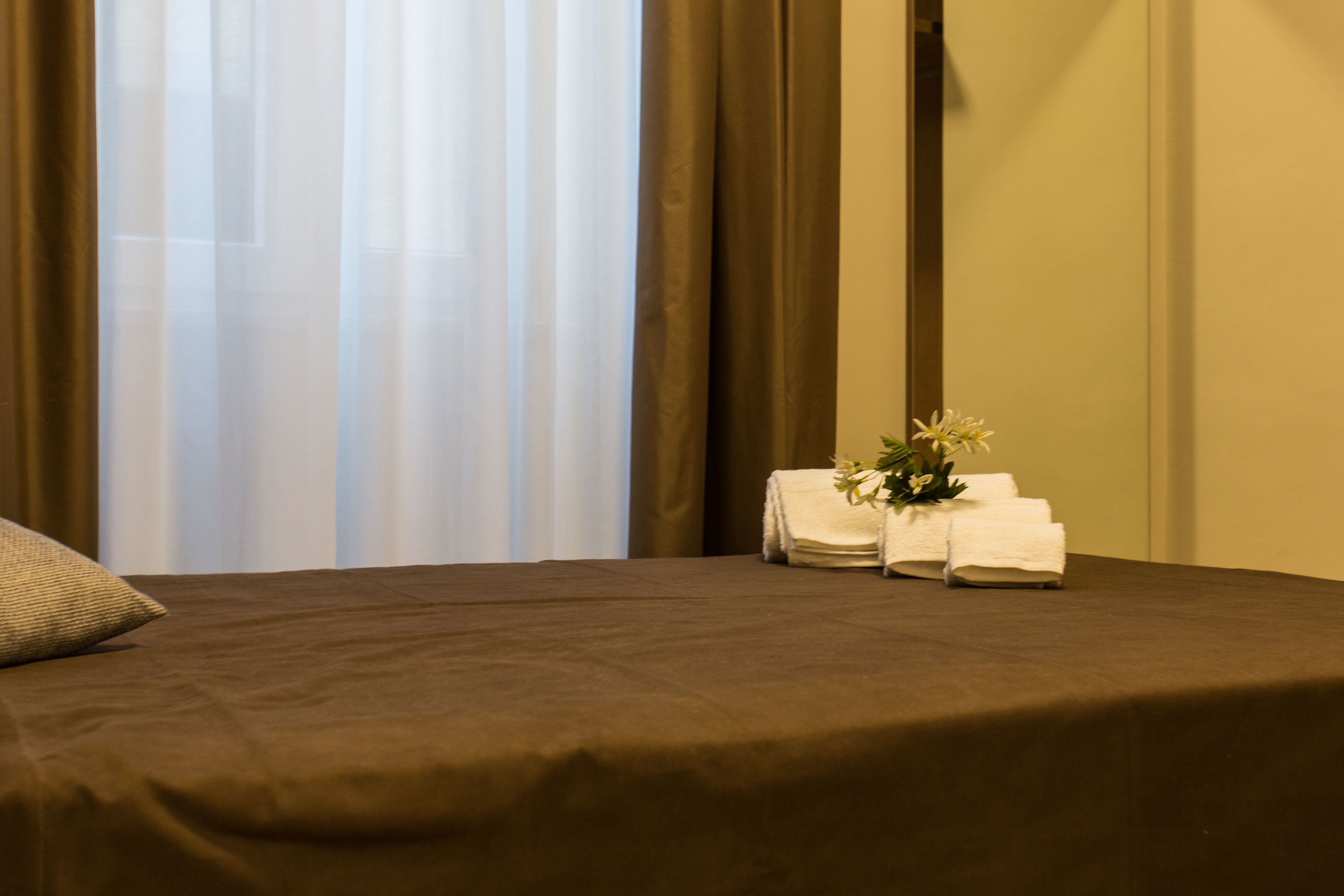 A neatly made bed with a brown bedspread, a pillow, and a small arrangement of white towels and flowers on the side.