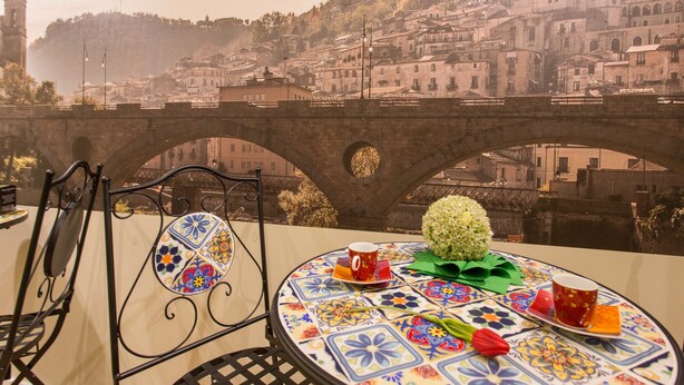 A table with a colorful tablecloth, a potted plant, and a cup, overlooking a historic town with a bridge. - Le Affacciate Bruzie Home (Cosenza)