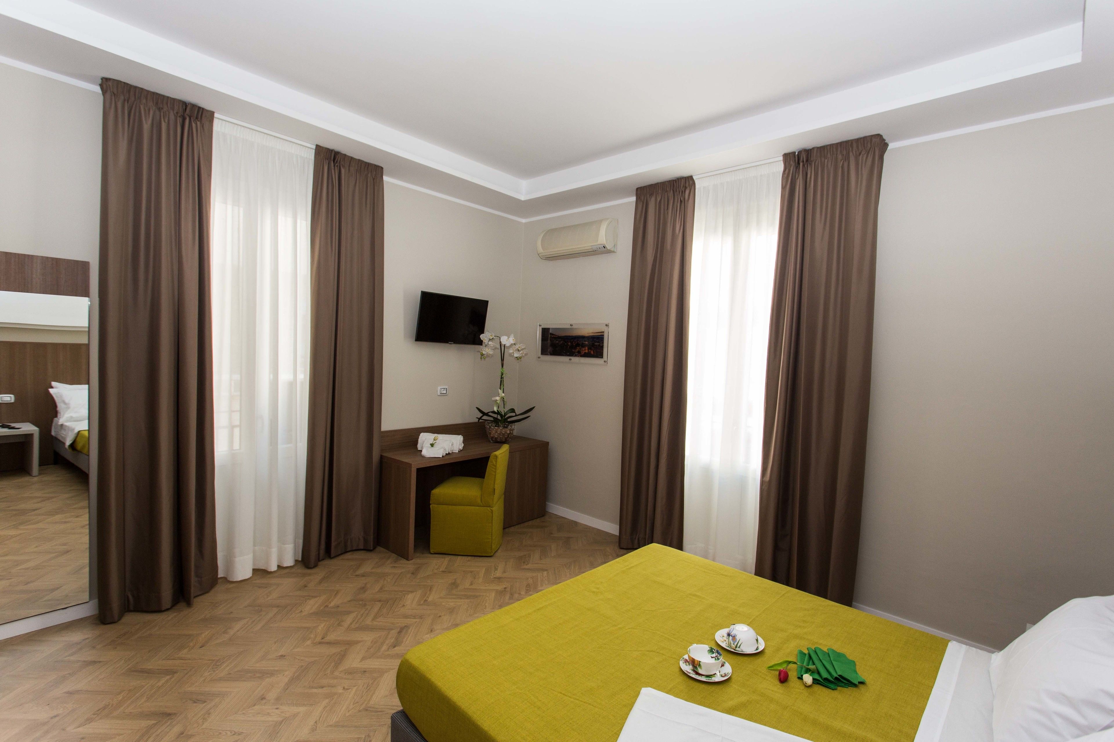 A hotel room with a bed, a desk, a chair, a television, and a window with curtains.