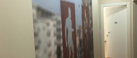 A hallway with a large abstract mural on the wall, a wooden floor, and a door with a number plate.