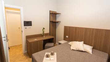 A neatly arranged bedroom with a bed, bedside table, and a desk area.