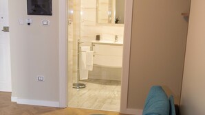 A room with a blue sofa, a wooden floor, a door leading to a bathroom, and a wall-mounted light switch. - Le Affacciate Bruzie Home (Cosenza)