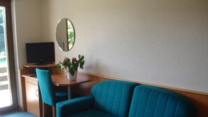 Una habitación con un sofá color turquesa, un escritorio de madera con una computadora, una silla y una planta en maceta.
