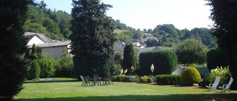 A grassy backyard with a lawn chair area, a tall coniferous tree, and a well-maintained hedge.