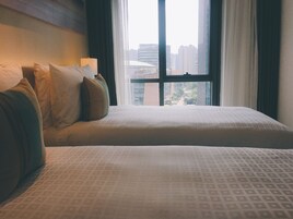 A hotel room with two beds, a window with a city view, and a lamp on the nightstand.