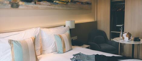 A hotel room with a neatly made bed, a chair, a small table with a globe and a camera, and a painting on the wall.