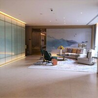 A modern living room with a sofa, chairs, and a coffee table. There is a large painting on the wall and a glass partition on the left.