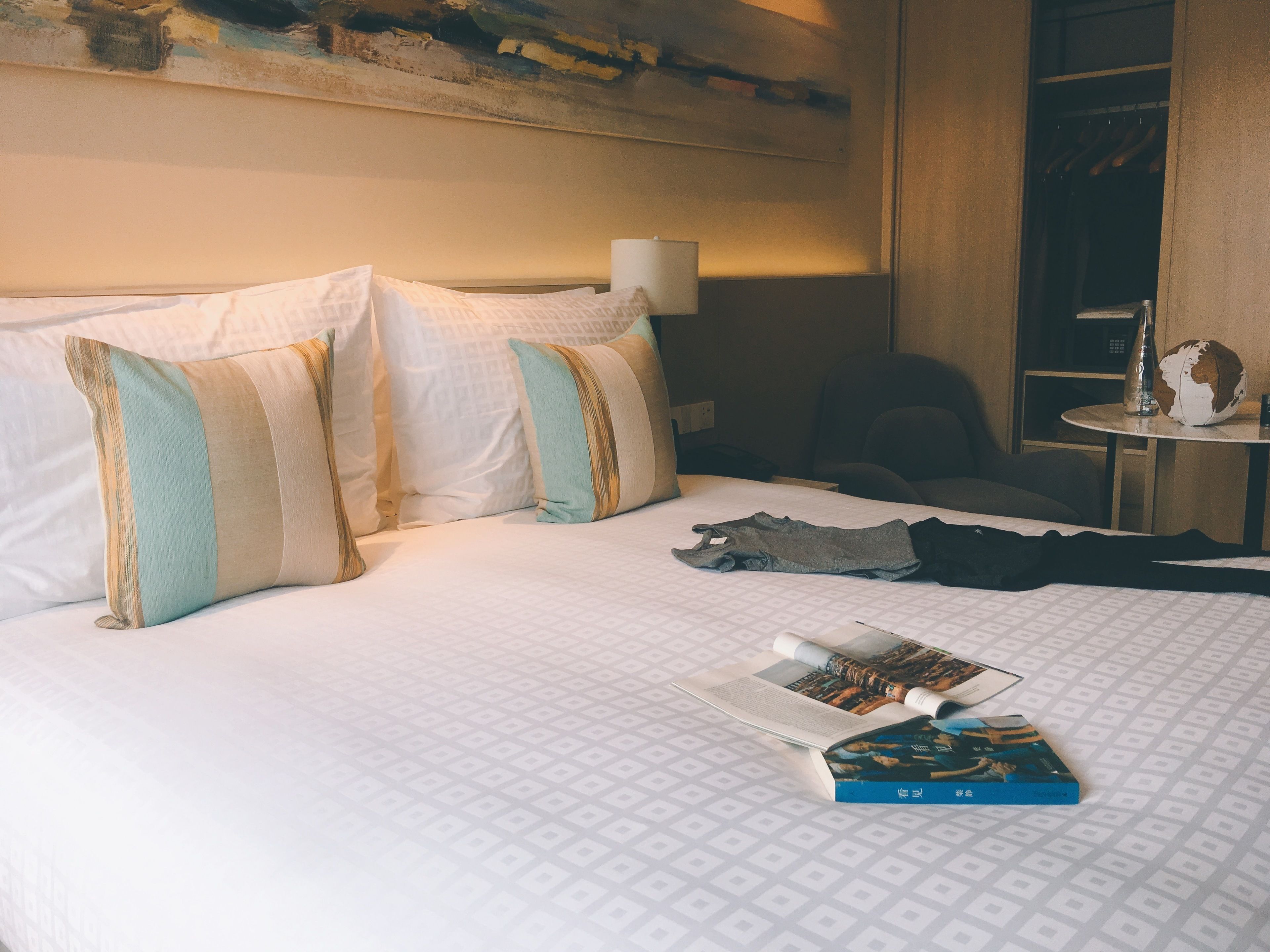 A hotel room with a neatly made bed, a small table with a lamp, and a chair.
