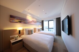 A hotel room with two beds, a large window, a painting on the wall, and a flat-screen TV.