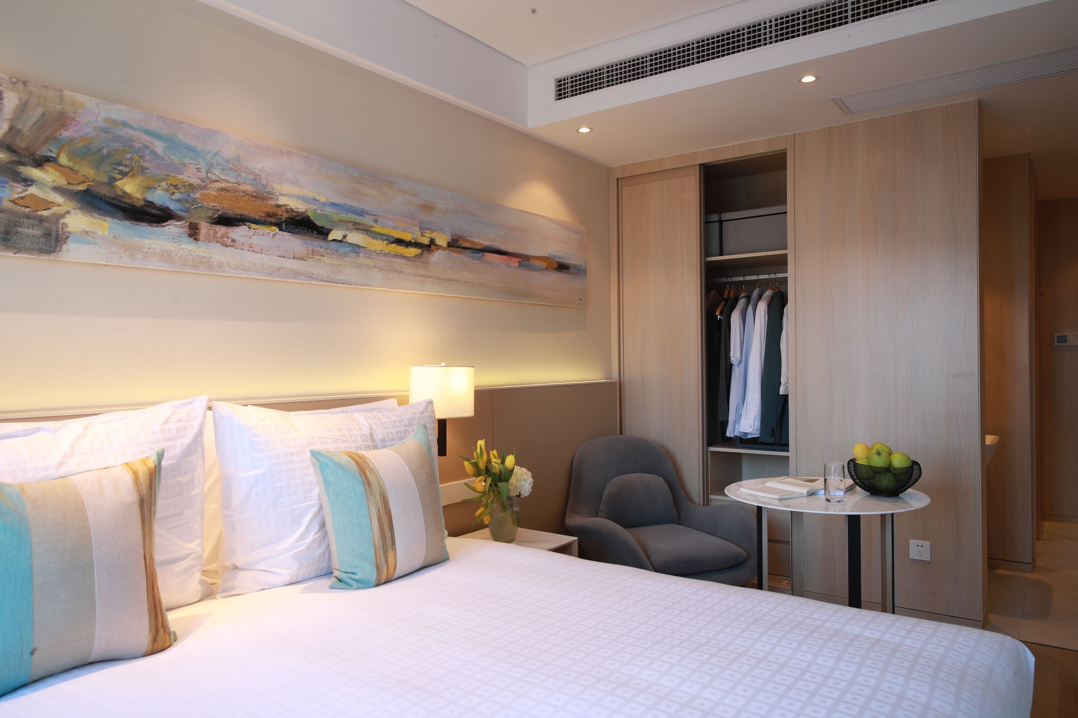 Une chambre d’hôtel avec un grand lit, un bureau avec une chaise, une petite table avec un panier de fruits et une armoire.