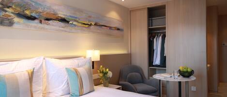 Une chambre d’hôtel avec un grand lit, un bureau avec une chaise, une petite table avec un panier de fruits et une armoire.