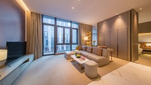 Quarto de hotel moderno com uma janela grande, um sofá, uma mesa de centro e uma TV.