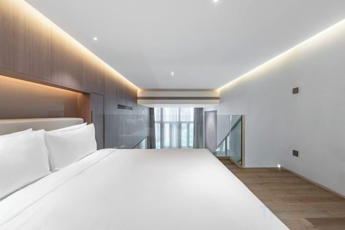 A modern hotel room with a large bed, a wooden headboard, and a view of a staircase.