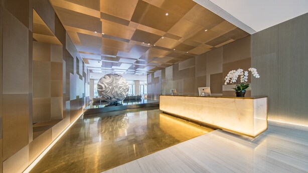 Um lobby de hotel moderno com um balcão de recepção, uma escultura decorativa na parede e uma orquídea em vaso.