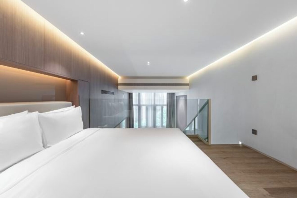 A modern bedroom with a large bed, wooden headboard, and a glass railing staircase.