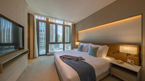 Quarto de hotel moderno com uma cama grande, televisão e vista para a cidade pelas janelas.