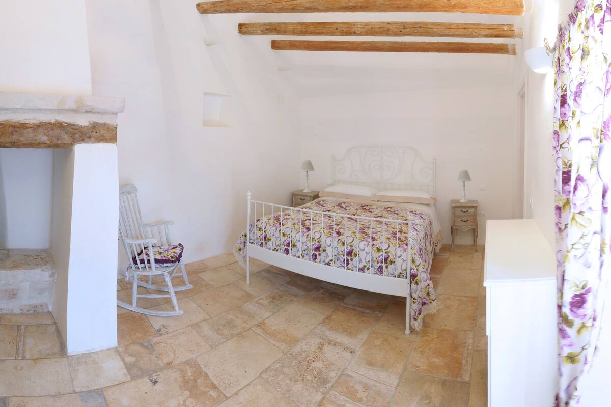 Une chambre avec un lit blanc, des poutres en bois, une chaise blanche et une petite table.