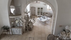 Een interieur met een boogvormige doorgang naar een eetruimte, met een tafel en stoelen, een wit kastje met glazen deuren en een kroonluchter.
