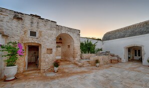 A courtyard with stone walls and a tiled roof, featuring a doorway and potted plants. - Masseria Luco (Martina Franca)