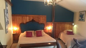 Un dormitorio con cabecera de madera, dos camas con ropa de cama blanca y almohadas rojas, una araña y una mesita de noche con lámpara.