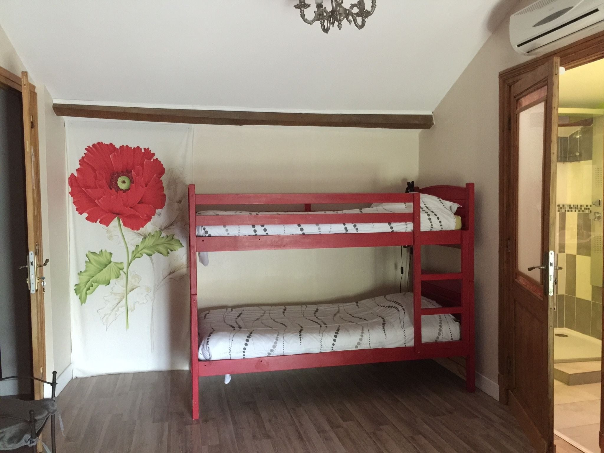 A bunk bed room with a red frame, a large red flower decoration on the wall, and a wooden floor.