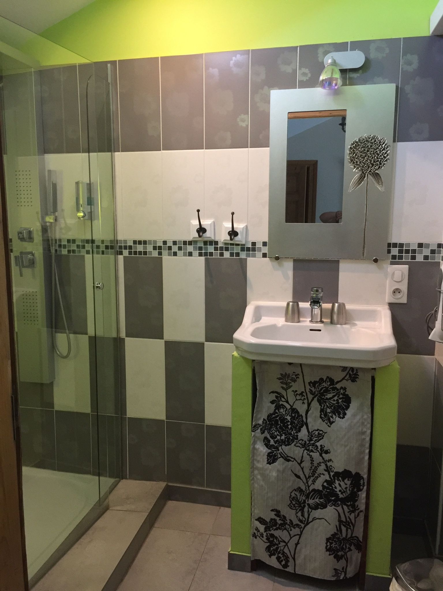 Un bagno con cabina doccia in vetro, lavabo con asciugamano a motivi floreali e specchio decorato con un fiore.