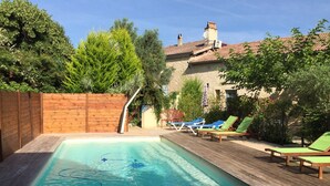 Una piscina rectangular con plataforma de madera y sillas de descanso.