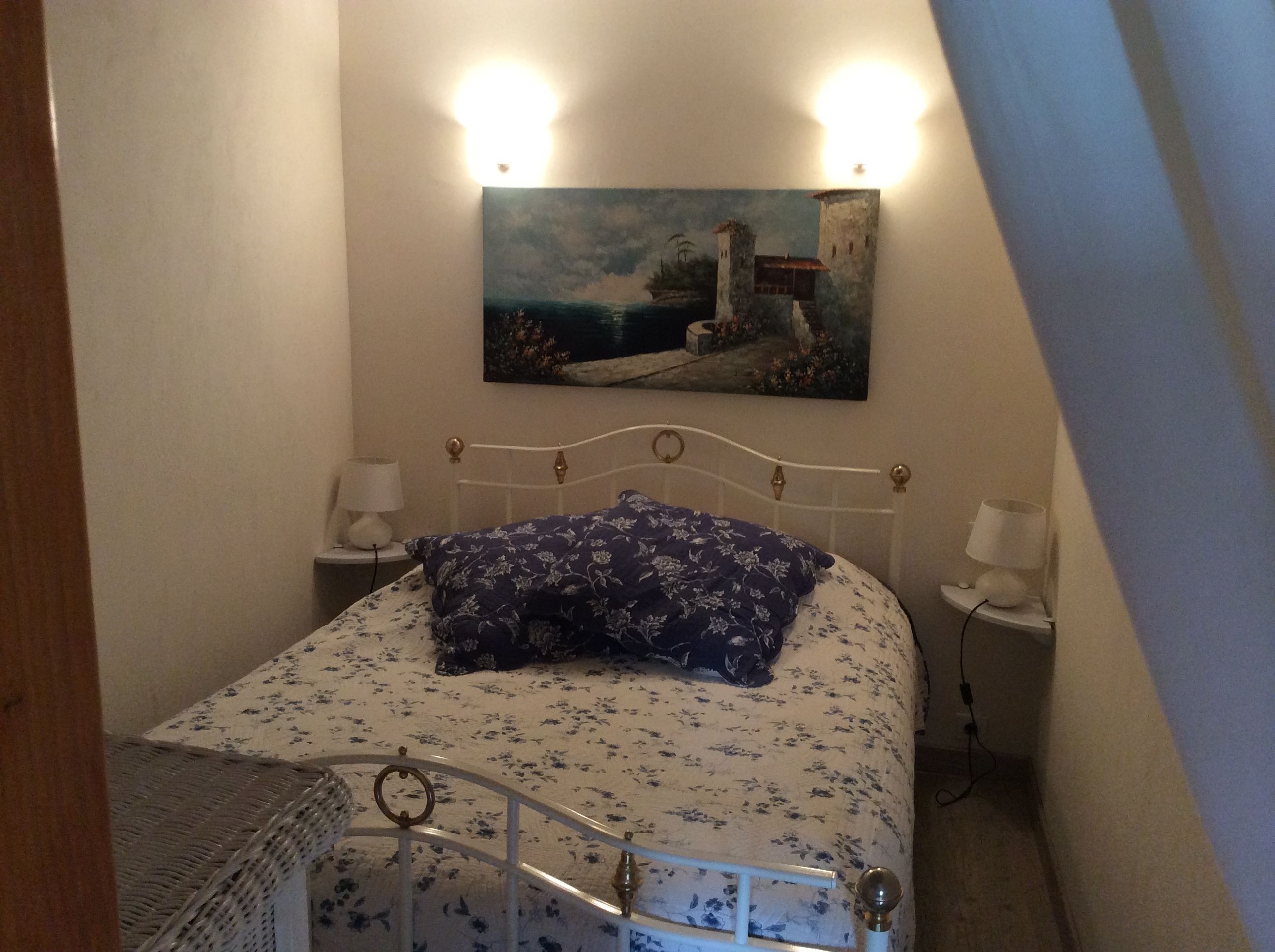 Un dormitorio con una cama, dos mesitas de noche, un cuadro en la pared y vistas al mar.