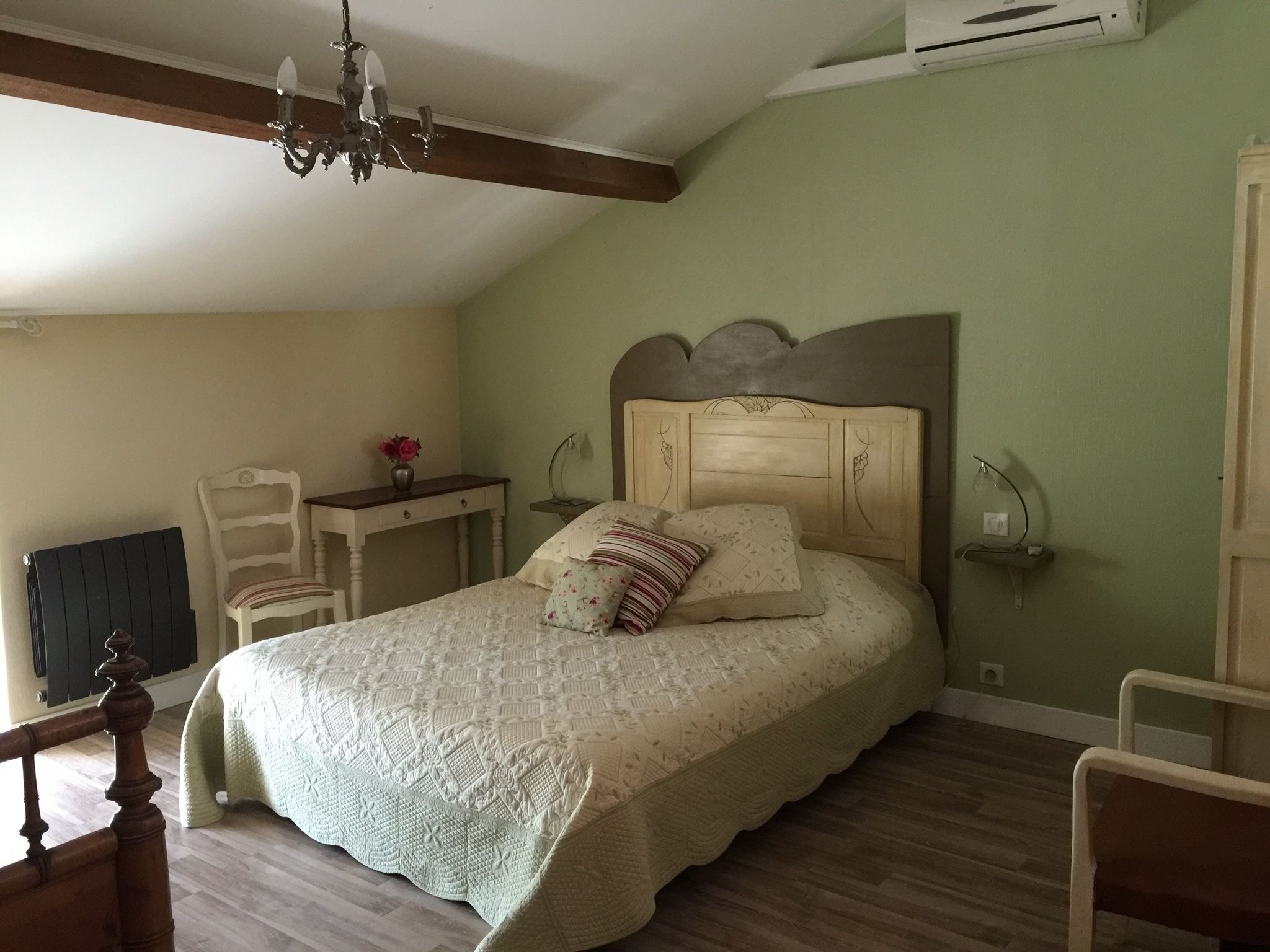 Un dormitorio con cama, escritorio, silla, candelabro y aire acondicionado.