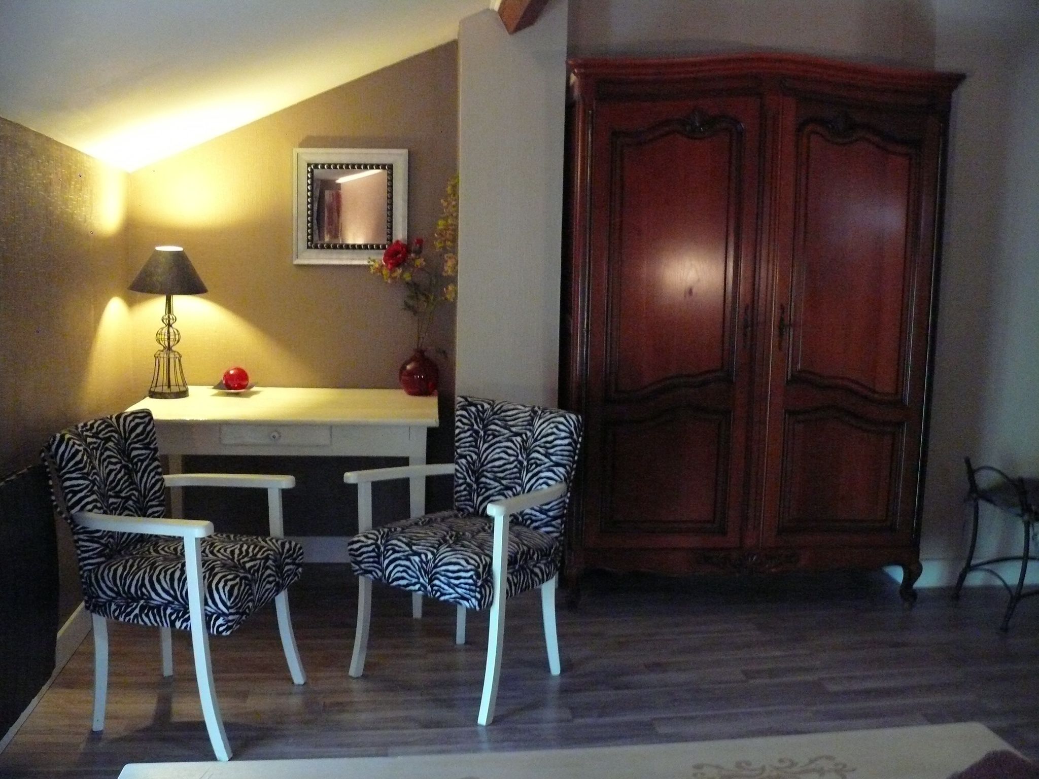 Una habitación con una mesa de comedor, dos sillas estampadas con motivos de cebra, una lámpara, un espejo y un armario de madera.