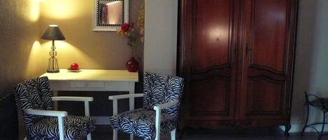 Una habitación con una mesa de comedor, dos sillas estampadas con motivos de cebra, una lámpara, un espejo y un armario de madera.