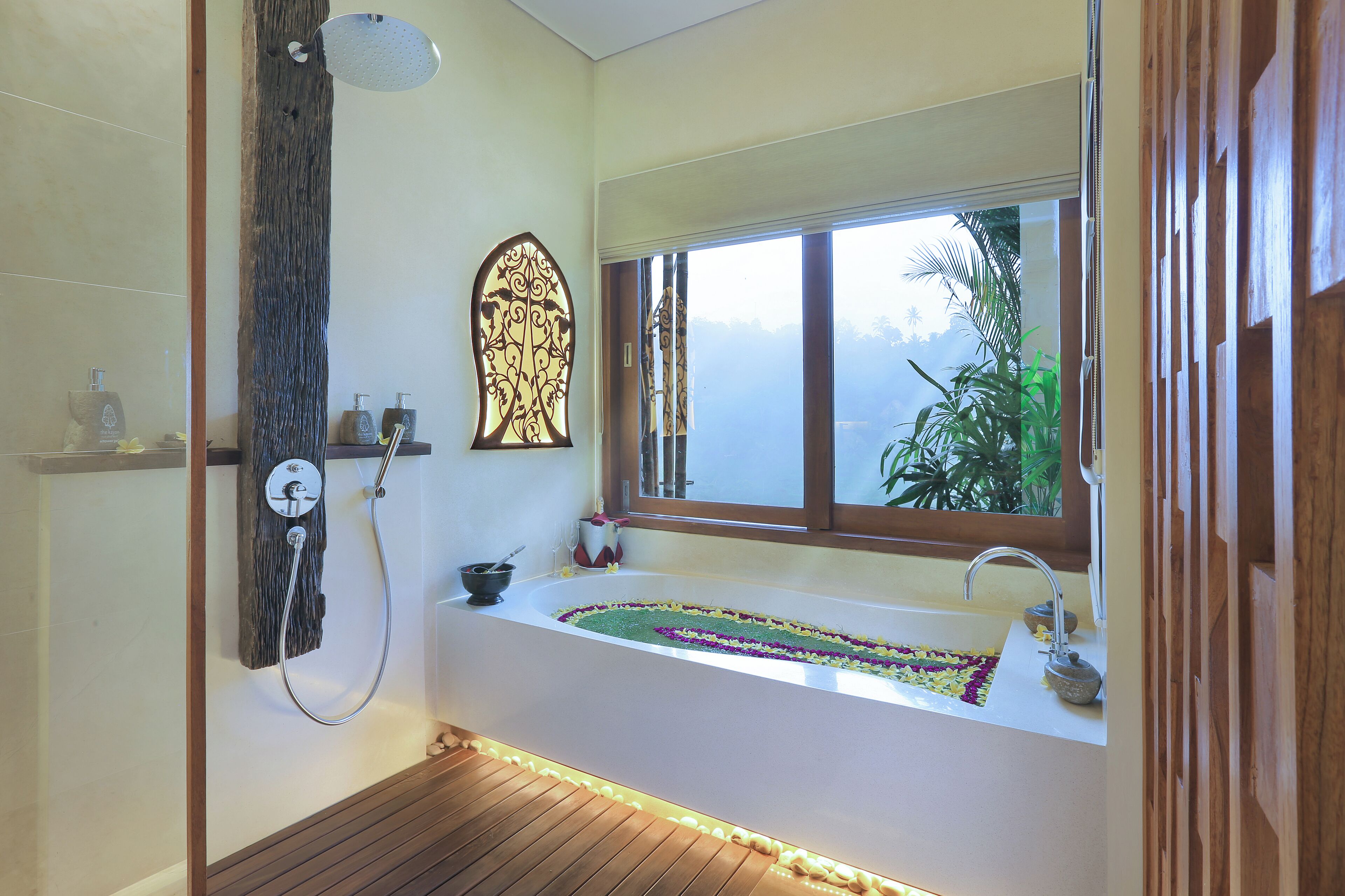 Un baño moderno con una bañera independiente, una ventana que da a zonas verdes, y suelo de madera.