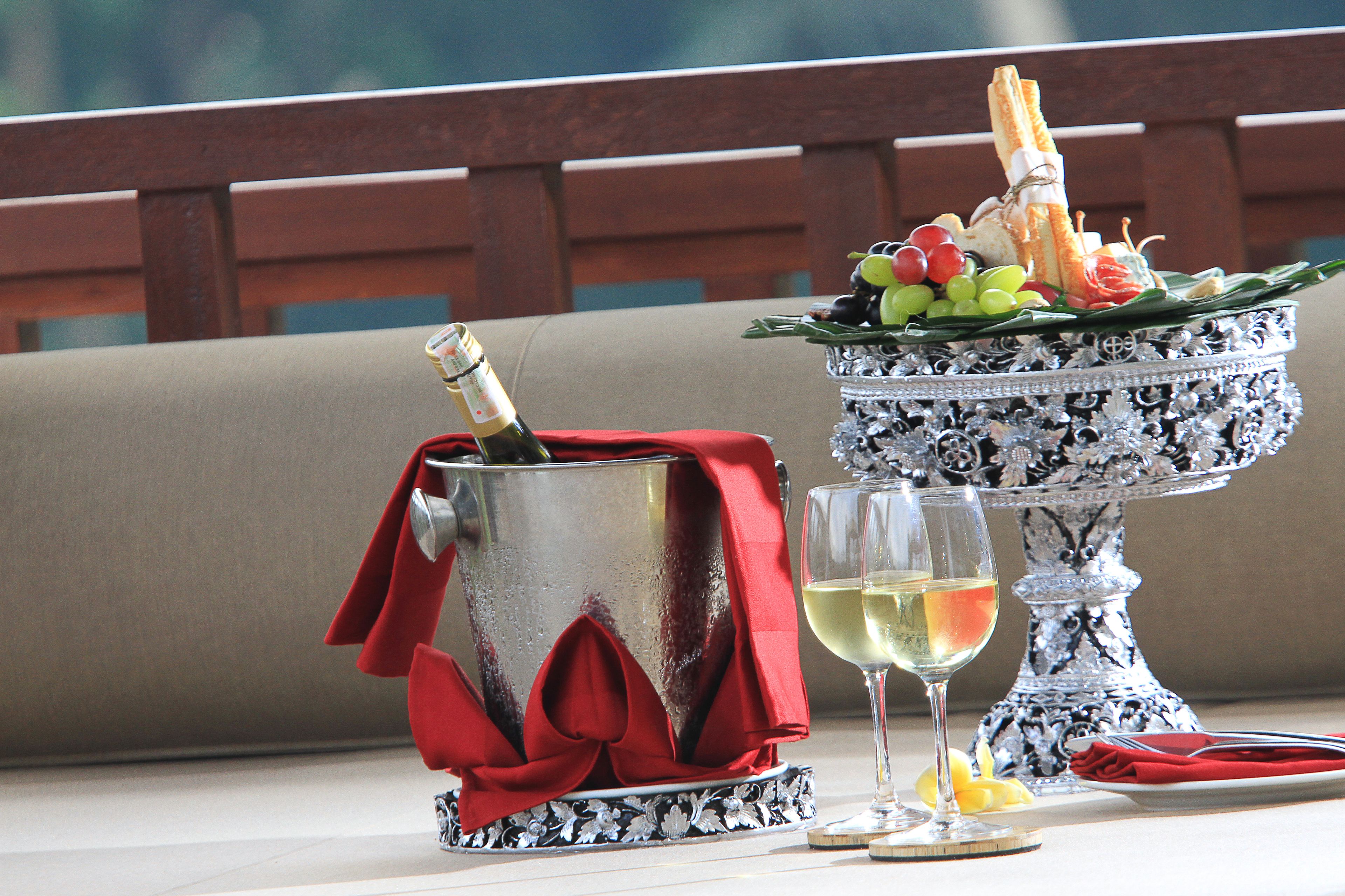 Een tafel met een champagnefles, een glas witte wijn en een decoratief zilveren schaal met fruit en brood.