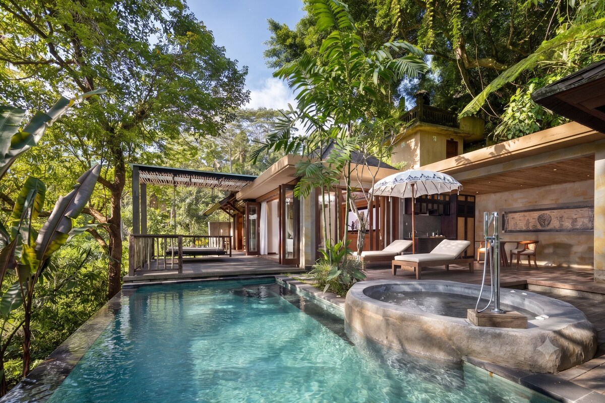 Un espace piscine doté d’un jacuzzi, de chaises longues et d’un coin salon abrité, le tout entouré d’une végétation luxuriante.