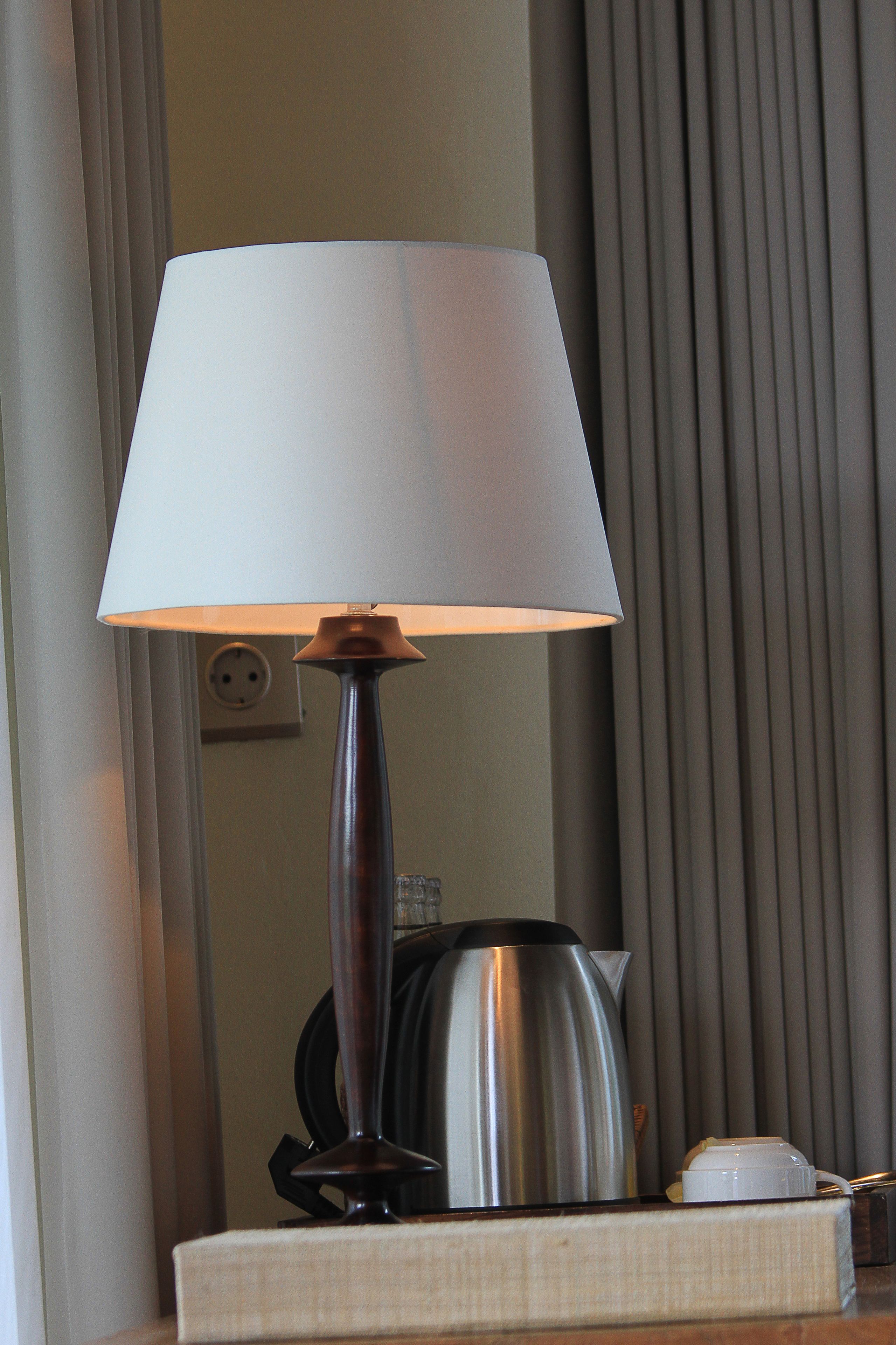 A lamp with a white shade on a table, a kettle, and a cup.