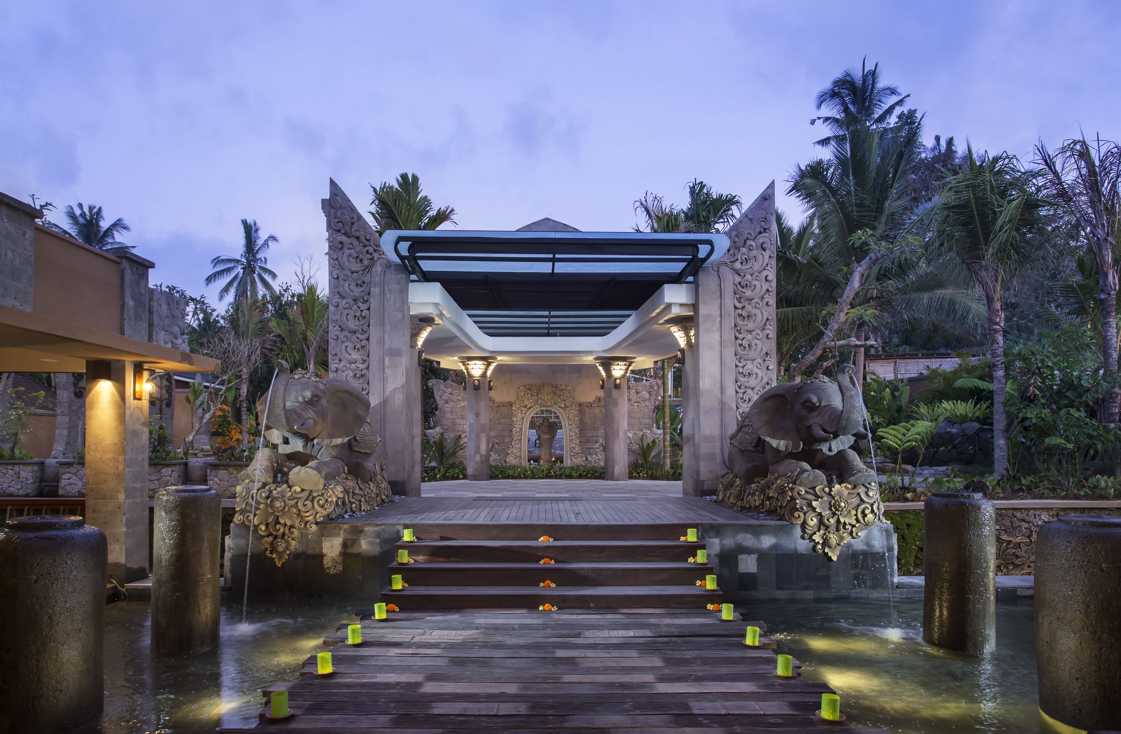 A stone entrance with a canopy, steps leading to a water feature, and palm trees in the background.