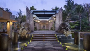 A stone entrance with a canopy, steps leading to a water feature, and palm trees in the background.