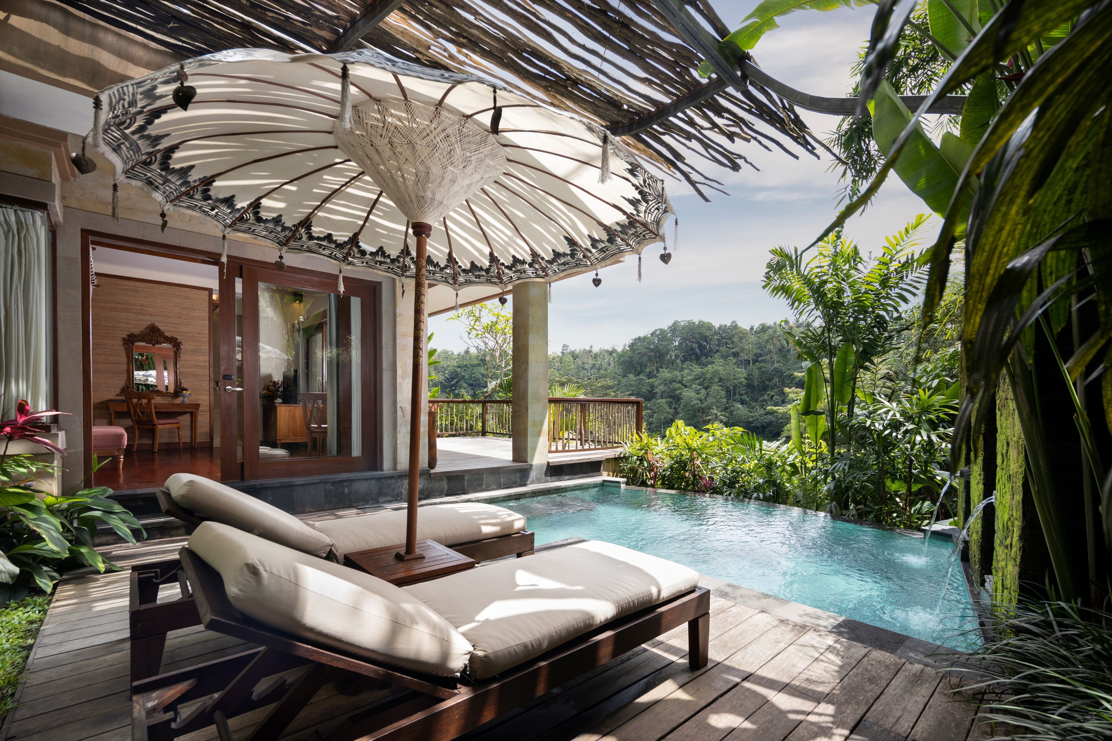 A poolside area with lounge chairs and a canopy, surrounded by lush greenery and a view of the landscape.