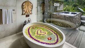 A spa area with a large bathtub surrounded by flowers, a shower area, and a stone wall with a plaque.