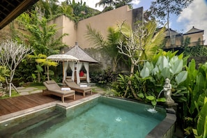 Relax by the serene pool surrounded by lush greenery and tropical plants, with lounge chairs and a gazebo for shade.