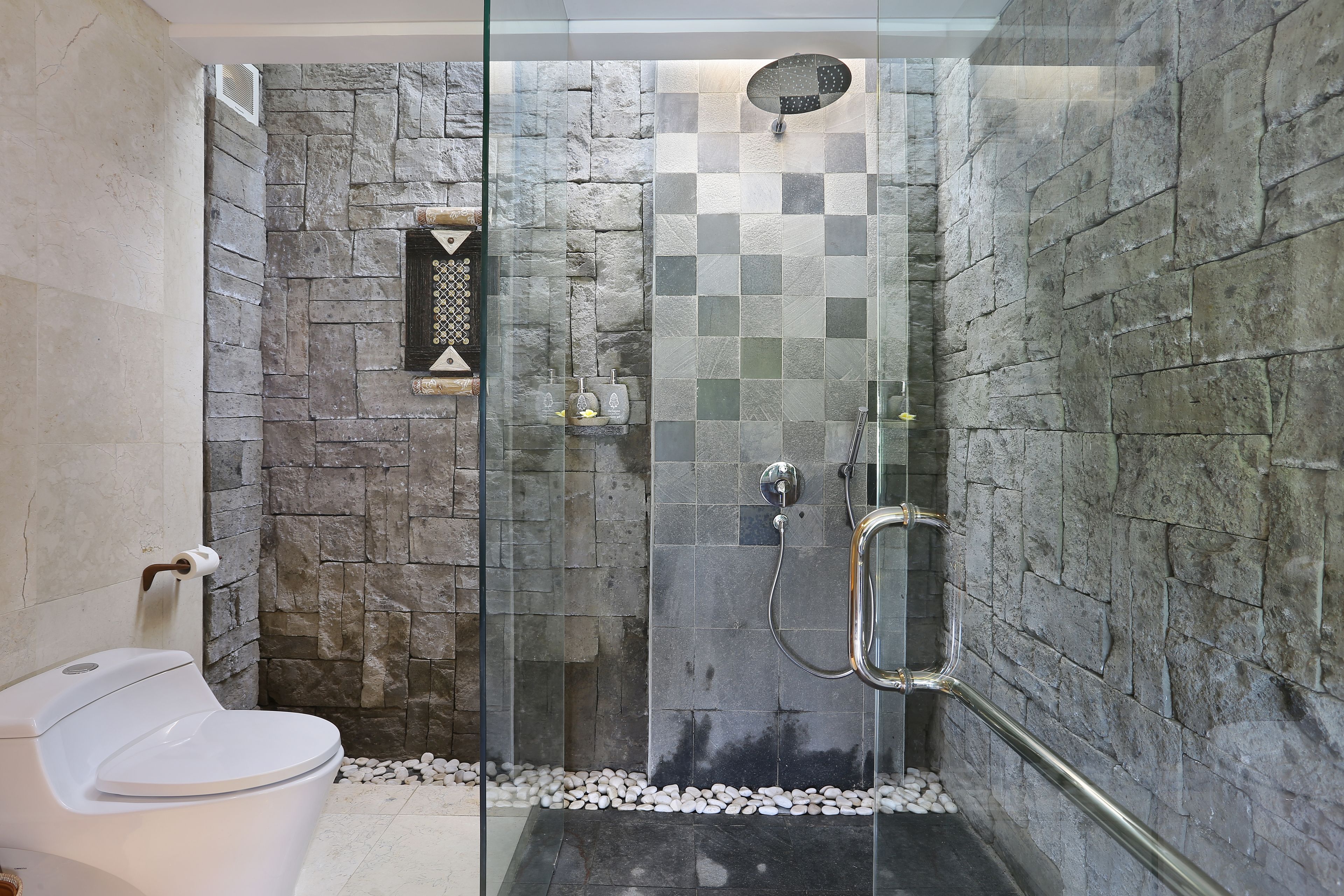 Un baño moderno con ducha de vidrio, paredes de piedra y un inodoro blanco.